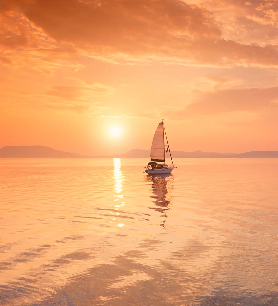 Sailboat crossing calm water at sunset